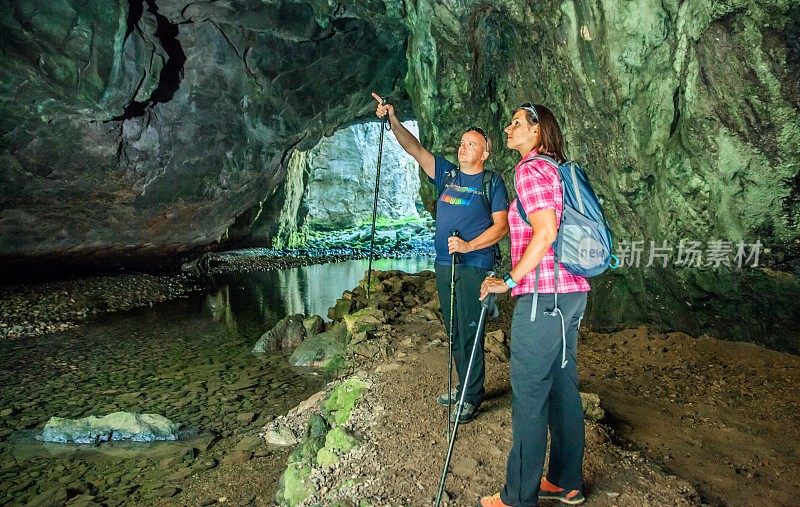 在斯洛文尼亚的Rakov Skocjan，一对游客夫妇在穿过大石头的隧道里，隧道里有一个水池